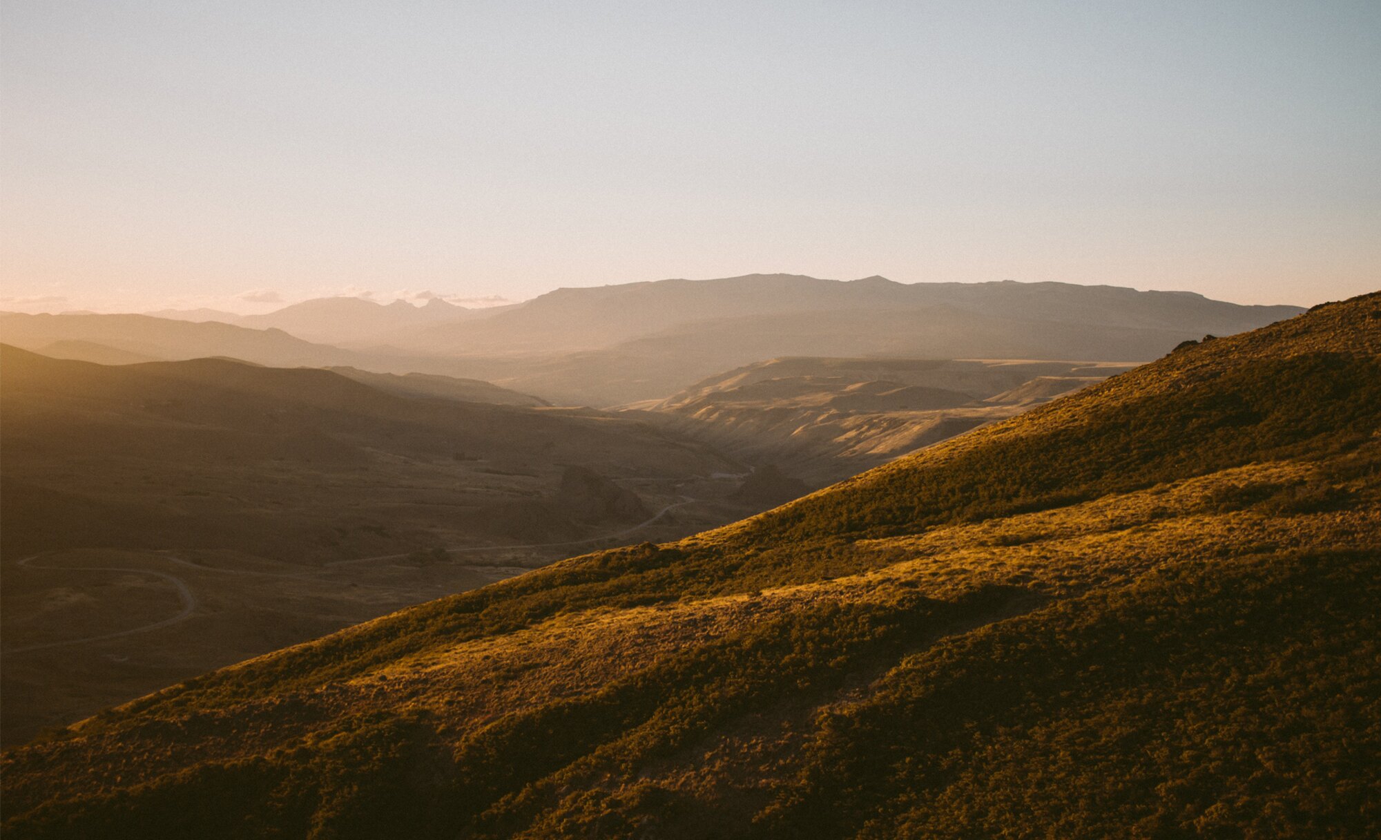 Dawn light over a Patagonian valley, mountains receding into golden mist